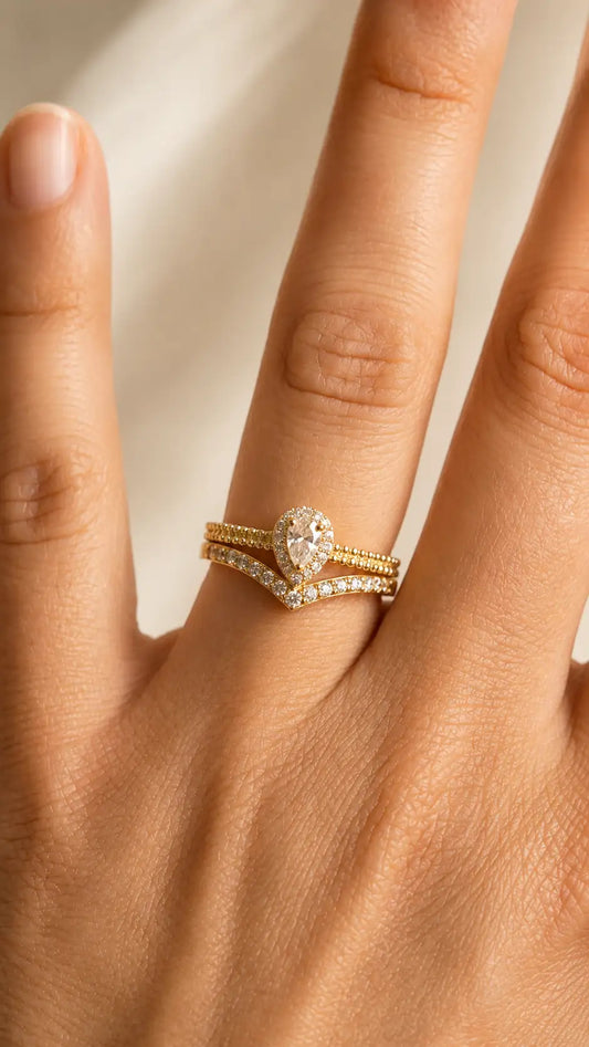 Hand wearing two gold rings with diamond accents on a neutral background