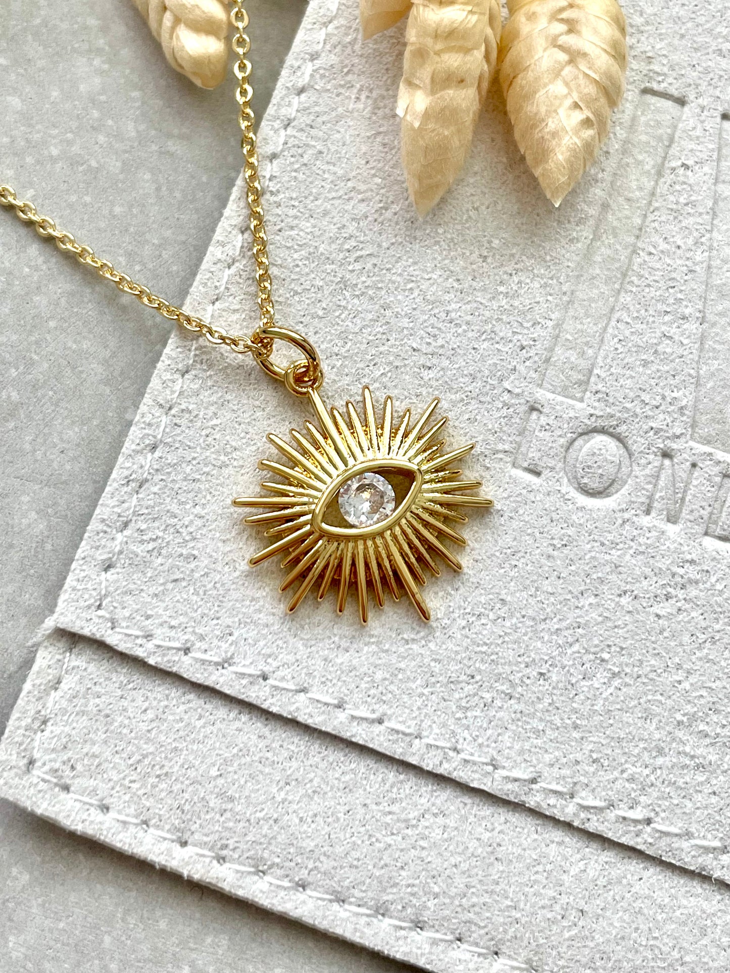 A gold-plated cubic zirconia necklace with a sun's eye pendant design, displayed on a white textured surface.