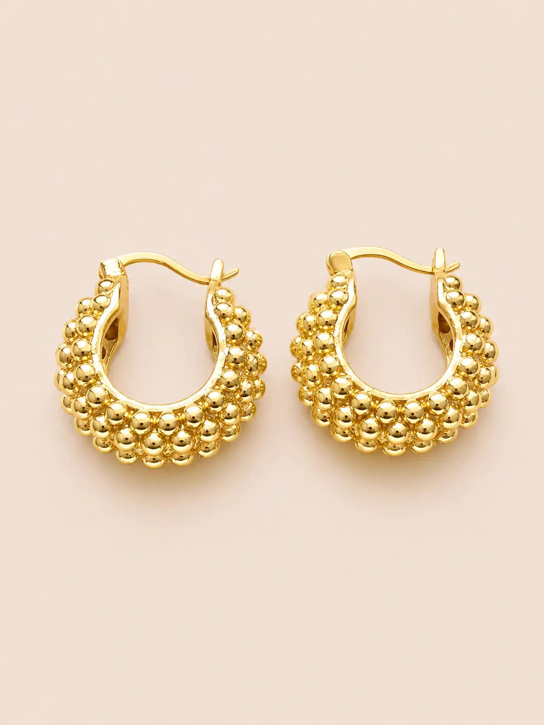 Gold hoop earrings with bead detailing on a beige background