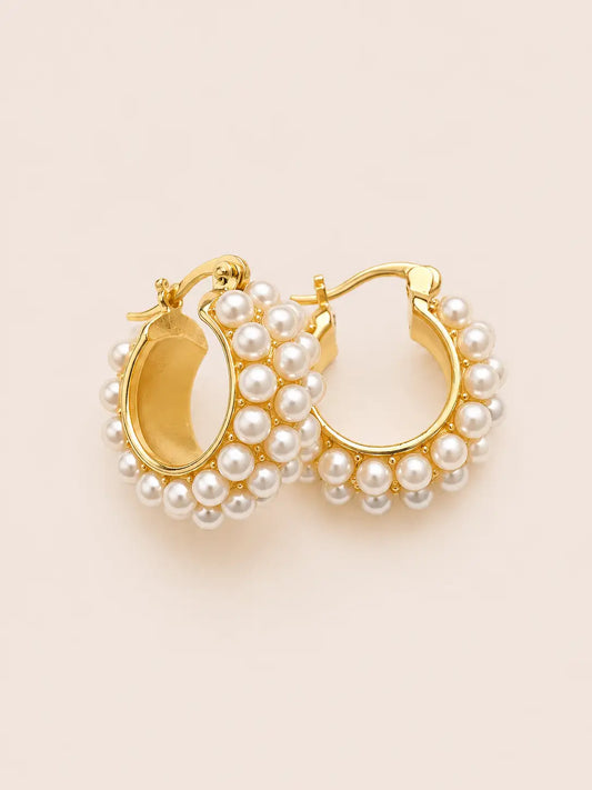 Gold hoop earrings with pearl accents on a beige background