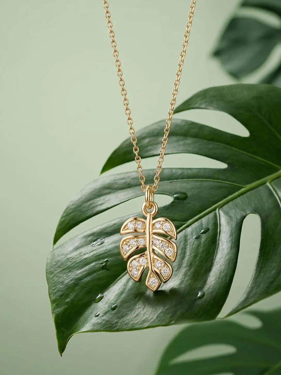 Gold leaf-shaped necklace with diamonds on a green leaf background