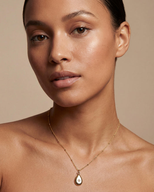 Woman wearing a gold necklace with a teardrop pendant against a beige background