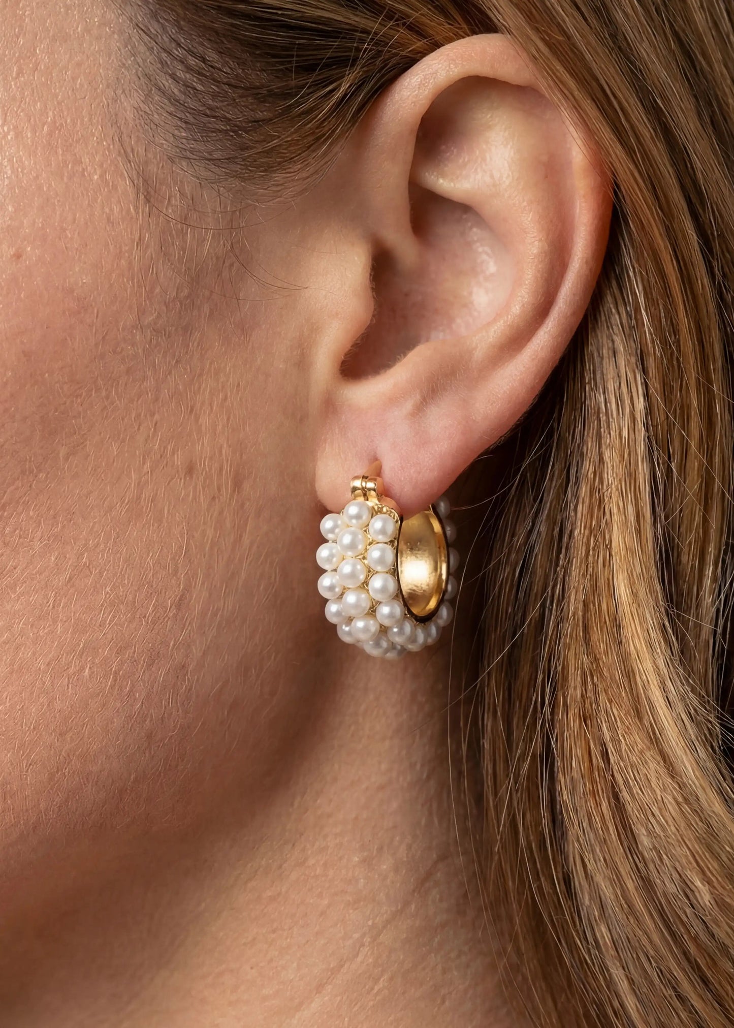 Close-up of an ear wearing a gold and pearl earring.