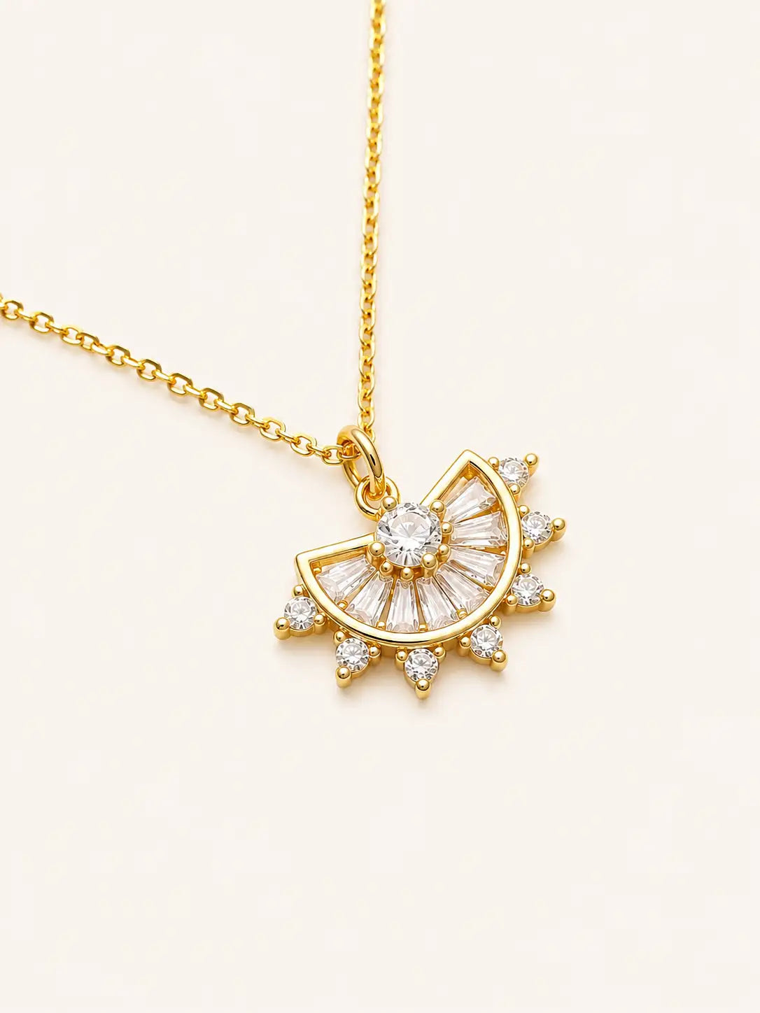 Gold necklace with a sun-shaped pendant on a light beige background
