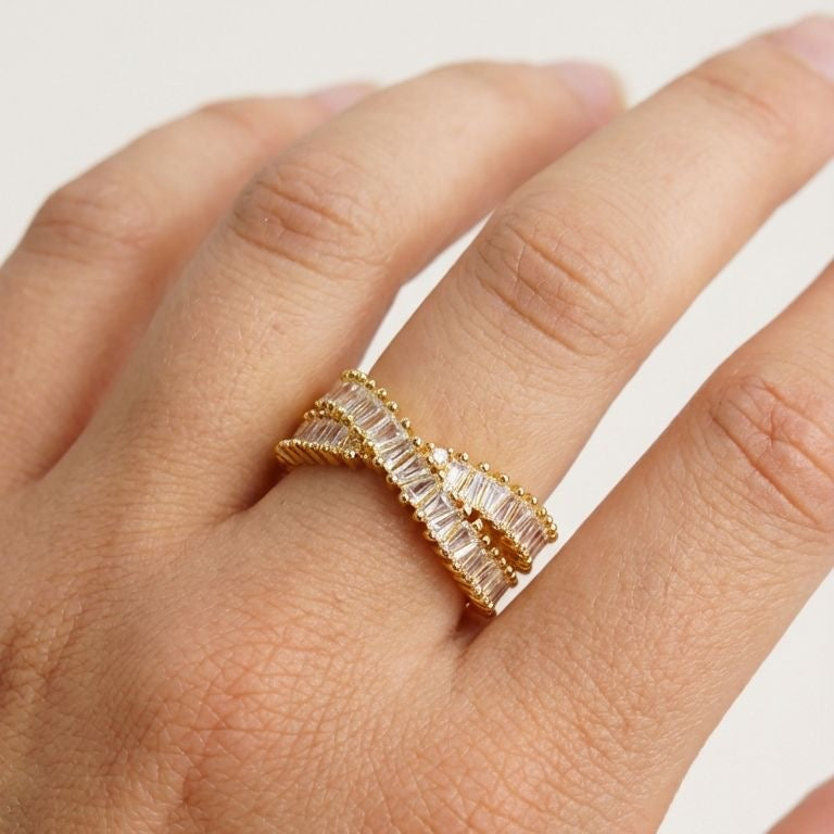 Gold ring with rectangular gemstones on a hand against a white background