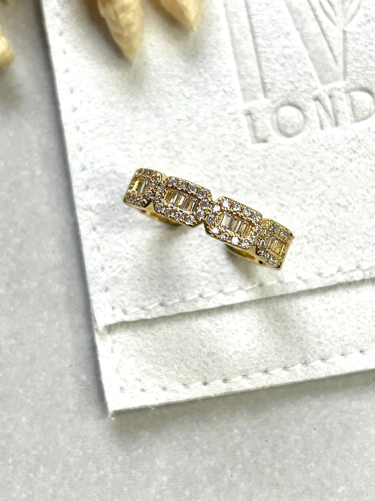 A gold-plated cubic zirconia baguette ring displayed on a white fabric surface with a blurred background.