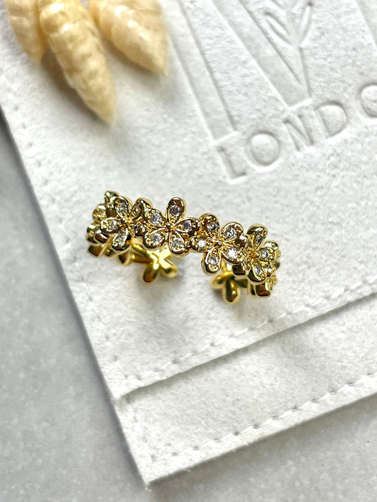 A gold-plated cubic zirconia daisy ring on a white textured surface, with a subtle shine.