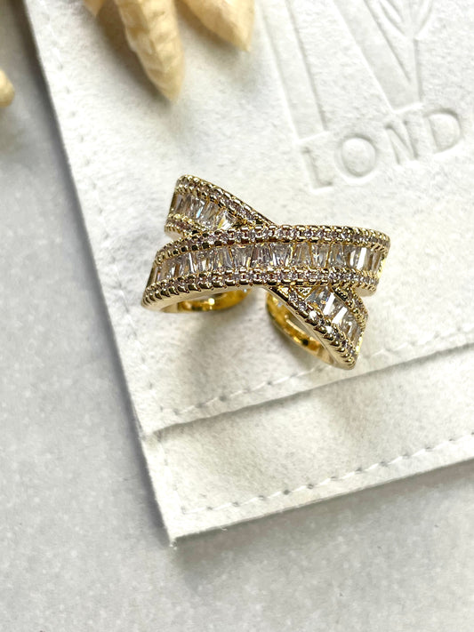An 18K gold plated cubic zirconia encrusted ring with a bow-shaped design, placed on a white fabric surface.