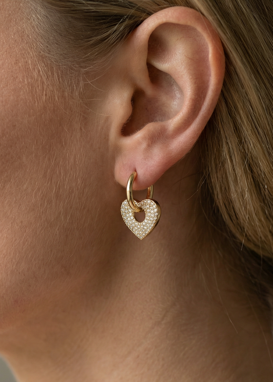 Close-up of a woman wearing a gold heart-shaped earring.Gold Plated Cubic Zirconia Heart Earrings - Ava