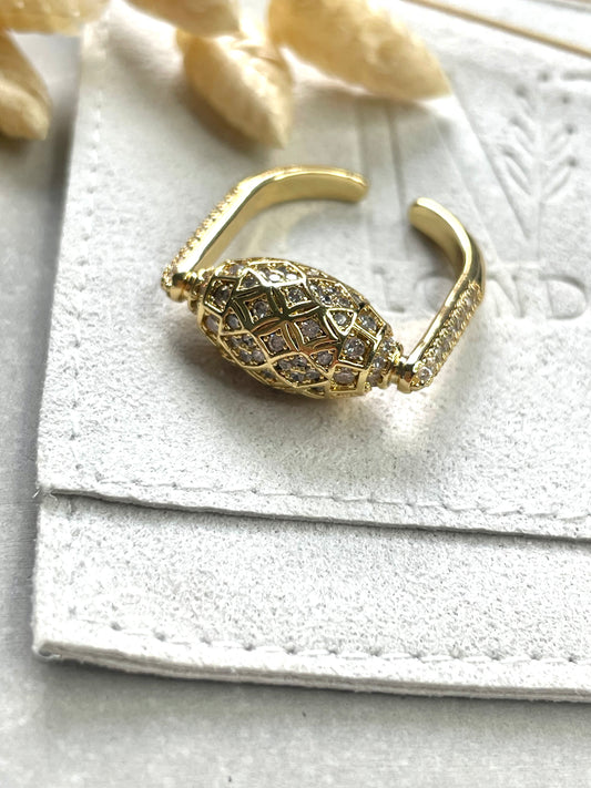 A gold-plated cubic zirconia mosaic ring on a white textured surface, with decorative stones nearby.