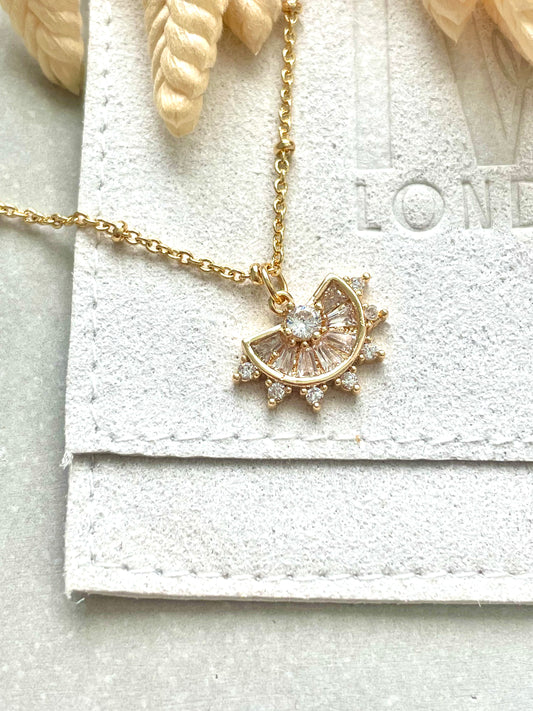 A gold-plated cubic zirconia necklace with a pendant and chain, displayed on a textured background.