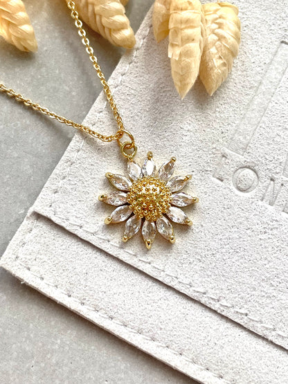 An 18k gold plated cubic zirconia sunflower pendant necklace with a chain and trigger clasp, displayed on a white textured background.