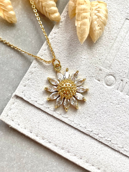 An 18k gold plated cubic zirconia sunflower pendant necklace with a chain and trigger clasp, displayed on a white textured background.
