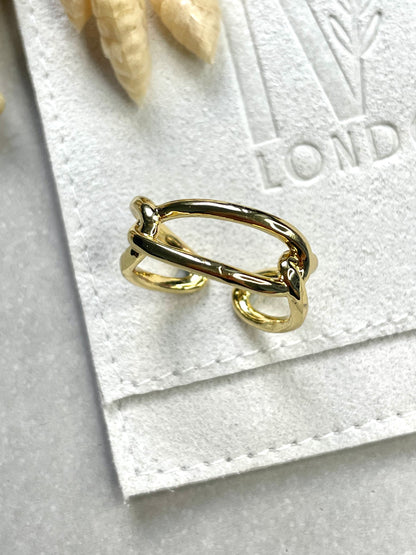 A gold-plated, brass knot-shaped ring on a white textured surface, possibly a card or fabric.