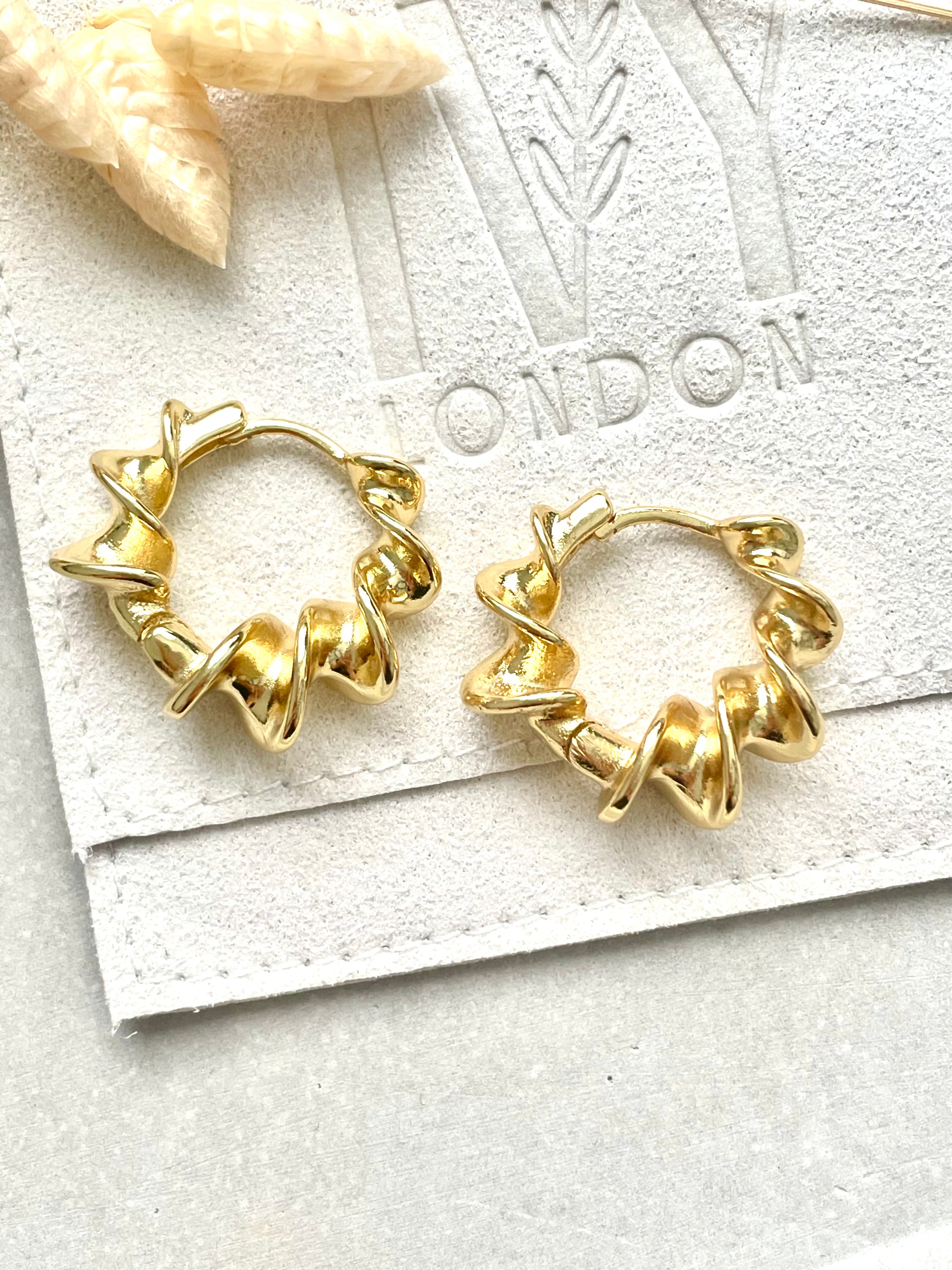 Gold plated twist earrings displayed on a white card with a star decoration in the background.