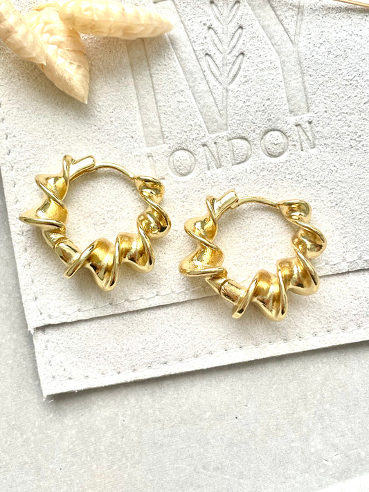 Gold plated twist earrings displayed on a white card with a star decoration in the background.
