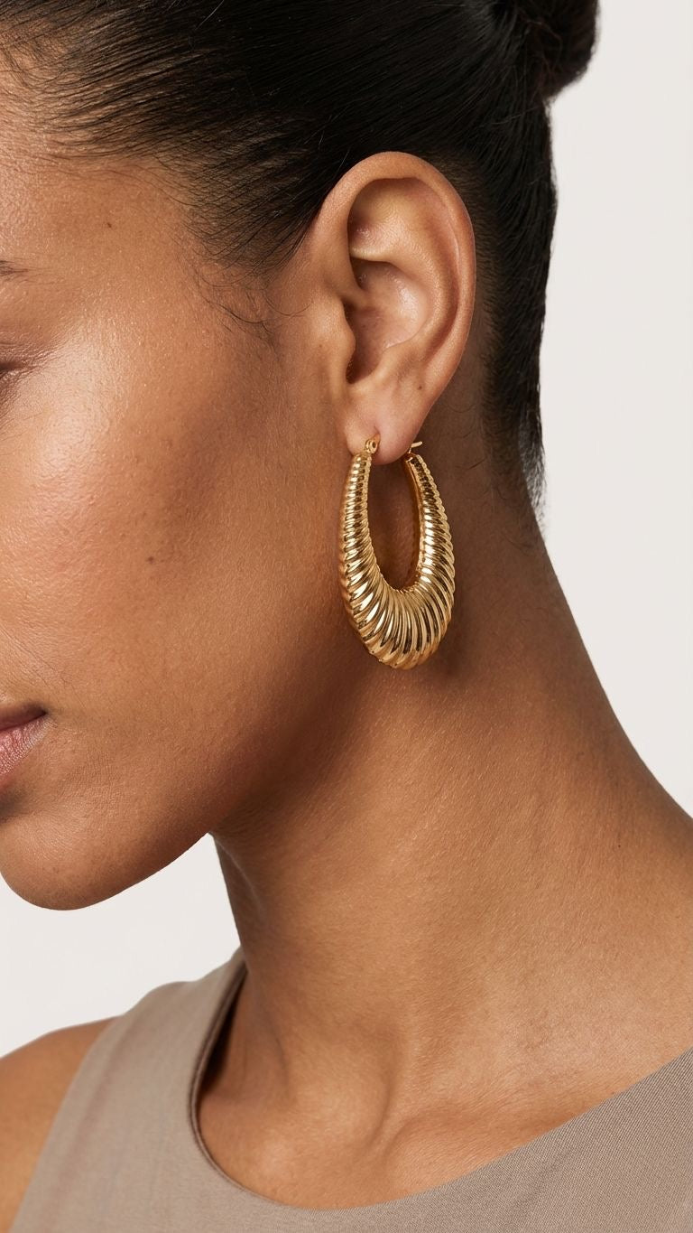 Close-up of a person wearing gold hoop earrings with a neutral background