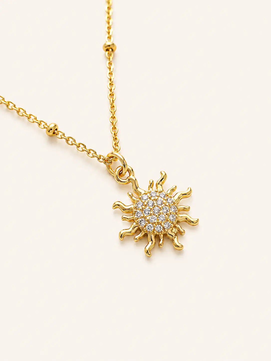 Gold sun-shaped pendant necklace on a light beige background