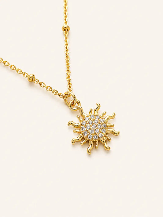 Gold sun-shaped pendant necklace on a light beige background