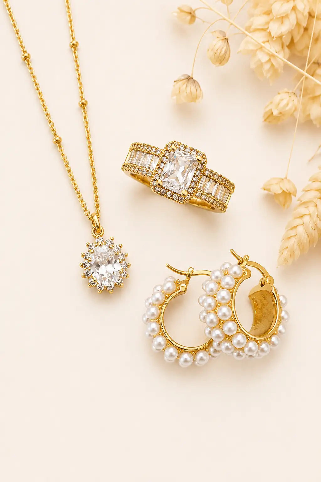 Gold jewelry set including necklace, ring, and earrings on a beige background with dried flowers.