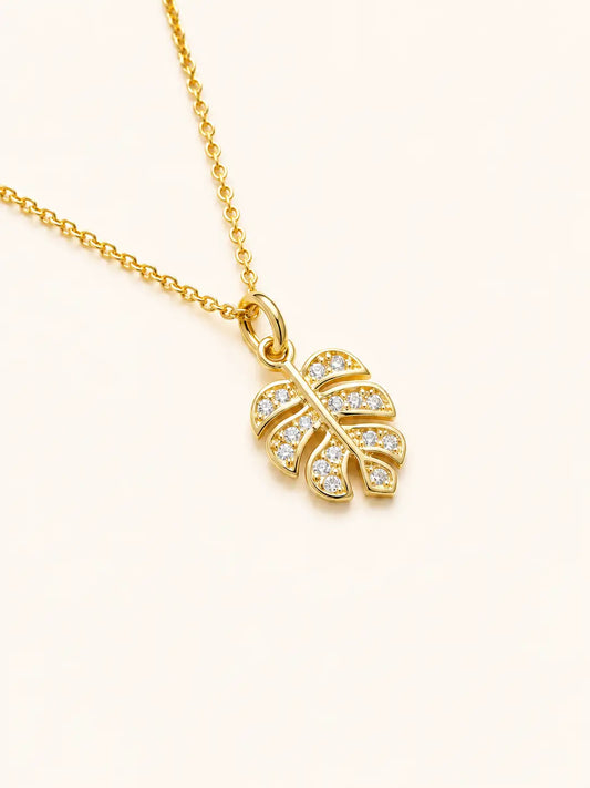 Gold necklace with a leaf-shaped pendant on a light beige background