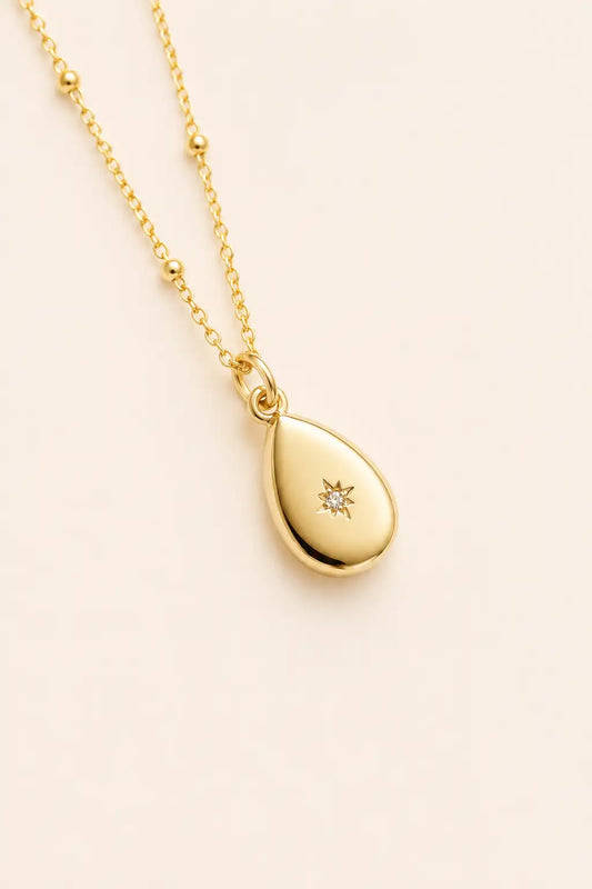 Gold teardrop pendant necklace with a diamond on a light beige background
