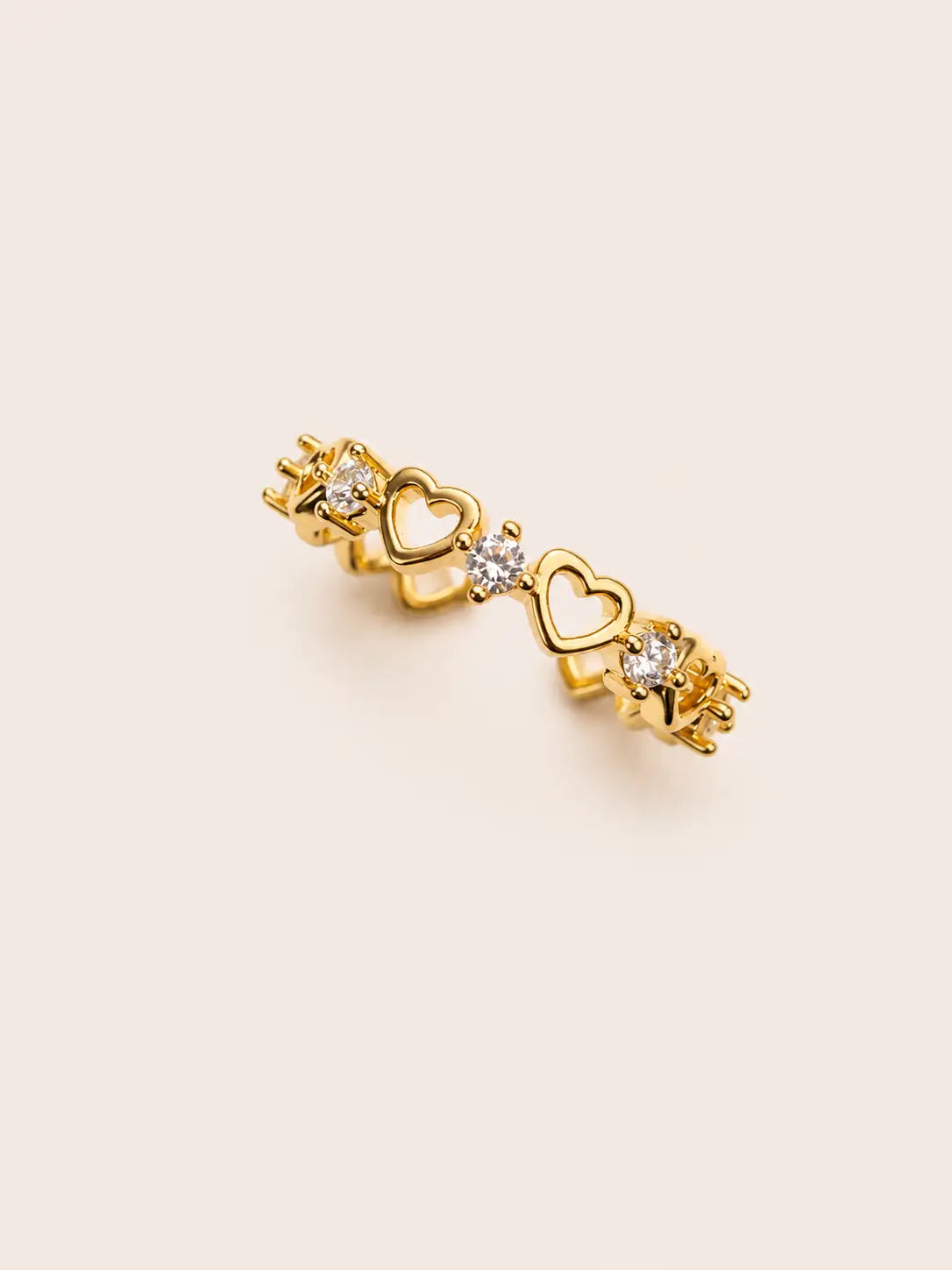 Gold earring with heart and star designs on a beige background