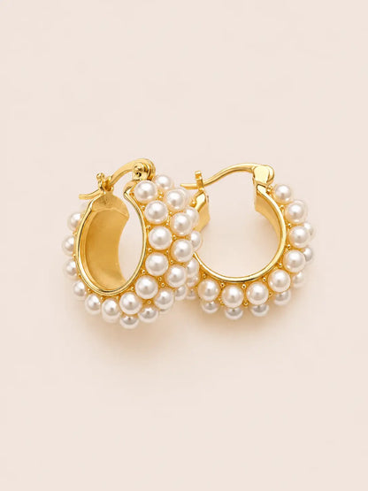 Gold hoop earrings with pearl accents on a beige background
