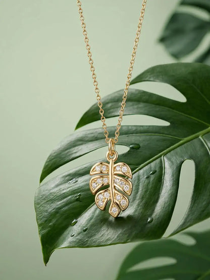 Gold leaf-shaped necklace with diamonds on a green leaf background