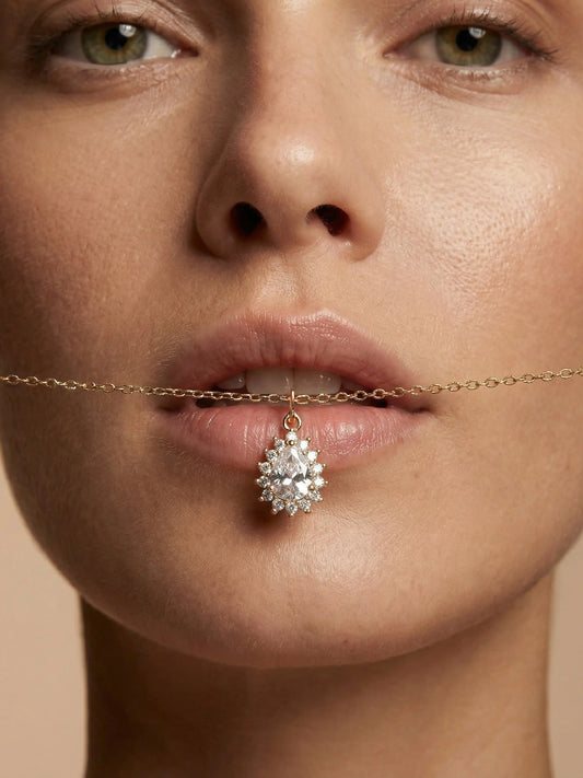 Close-up of a woman's face with a diamond necklace draped over her lips against a beige background
